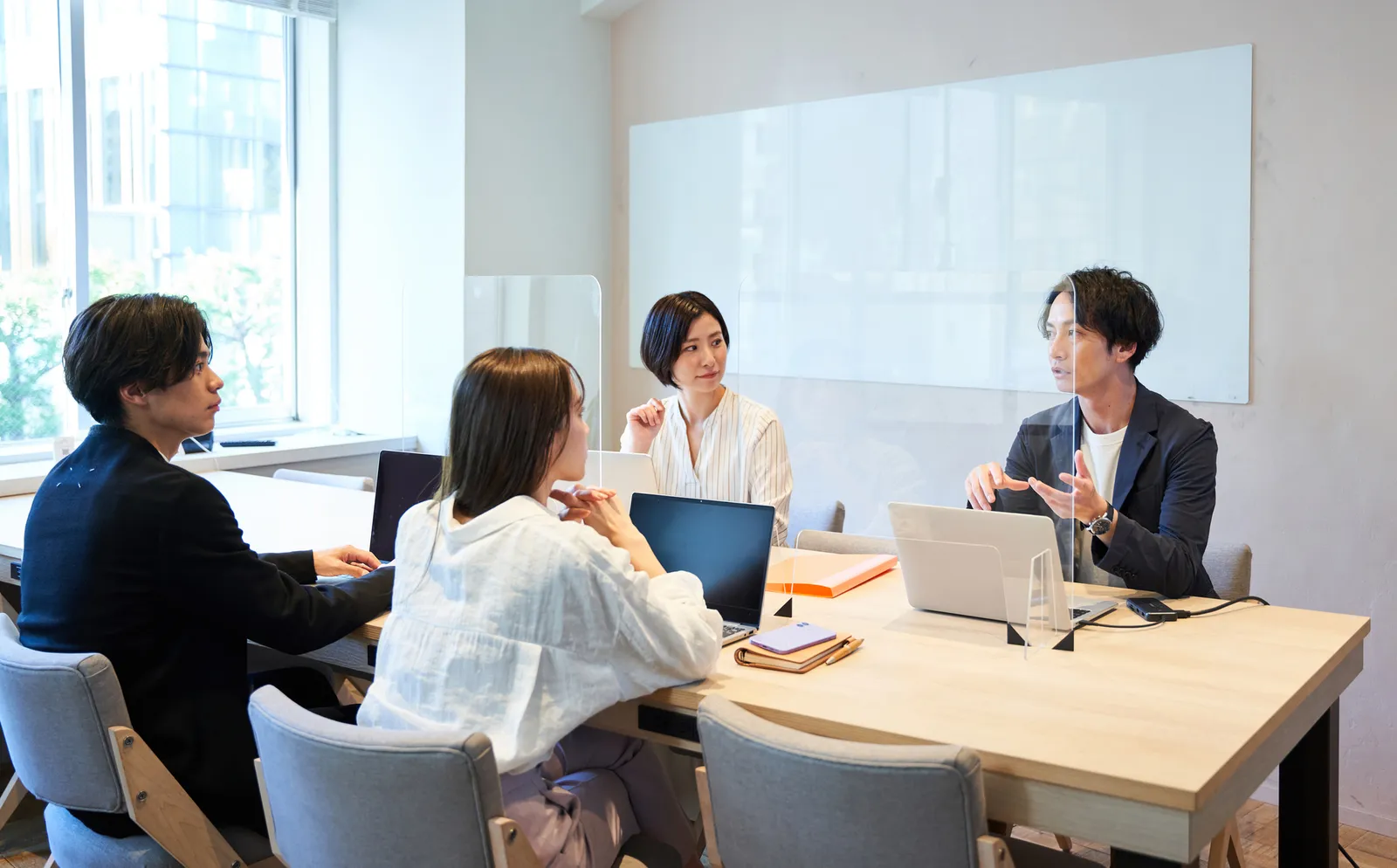 会議室でノートパソコンを囲んで話し合う四人の社員